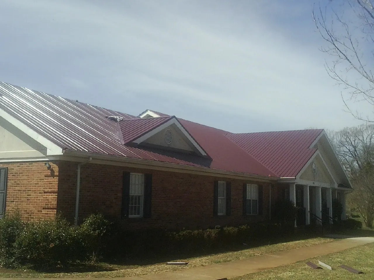Red metal roof with gabled entries on a long brick building, from a Hail Damage Roof Repair job in Castro Valley