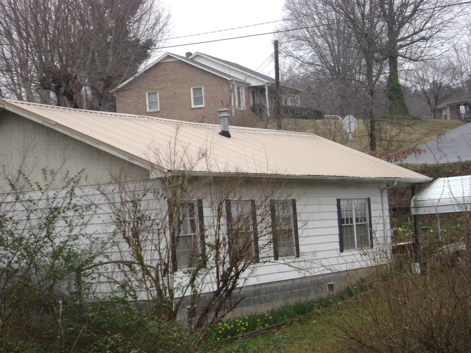 Tan metal roof on a white sided house set into a hillside — Commercial Roofing by Roofing Brothers in Castro Valley